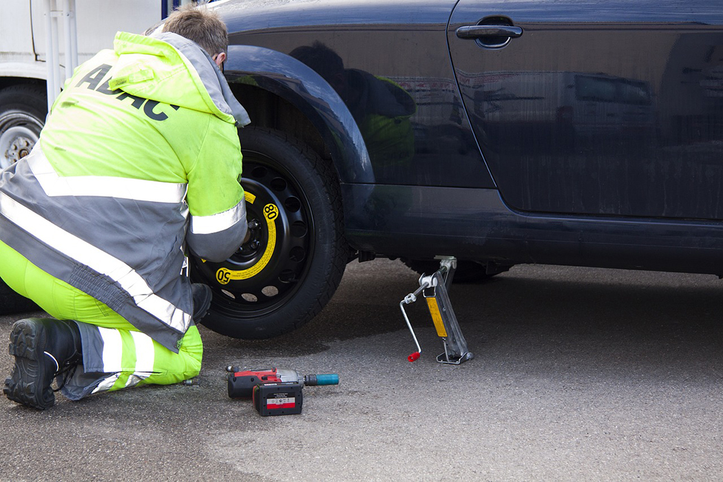 man attaching a spare tire using a emergency repair kit (car jack & drill with socket) 